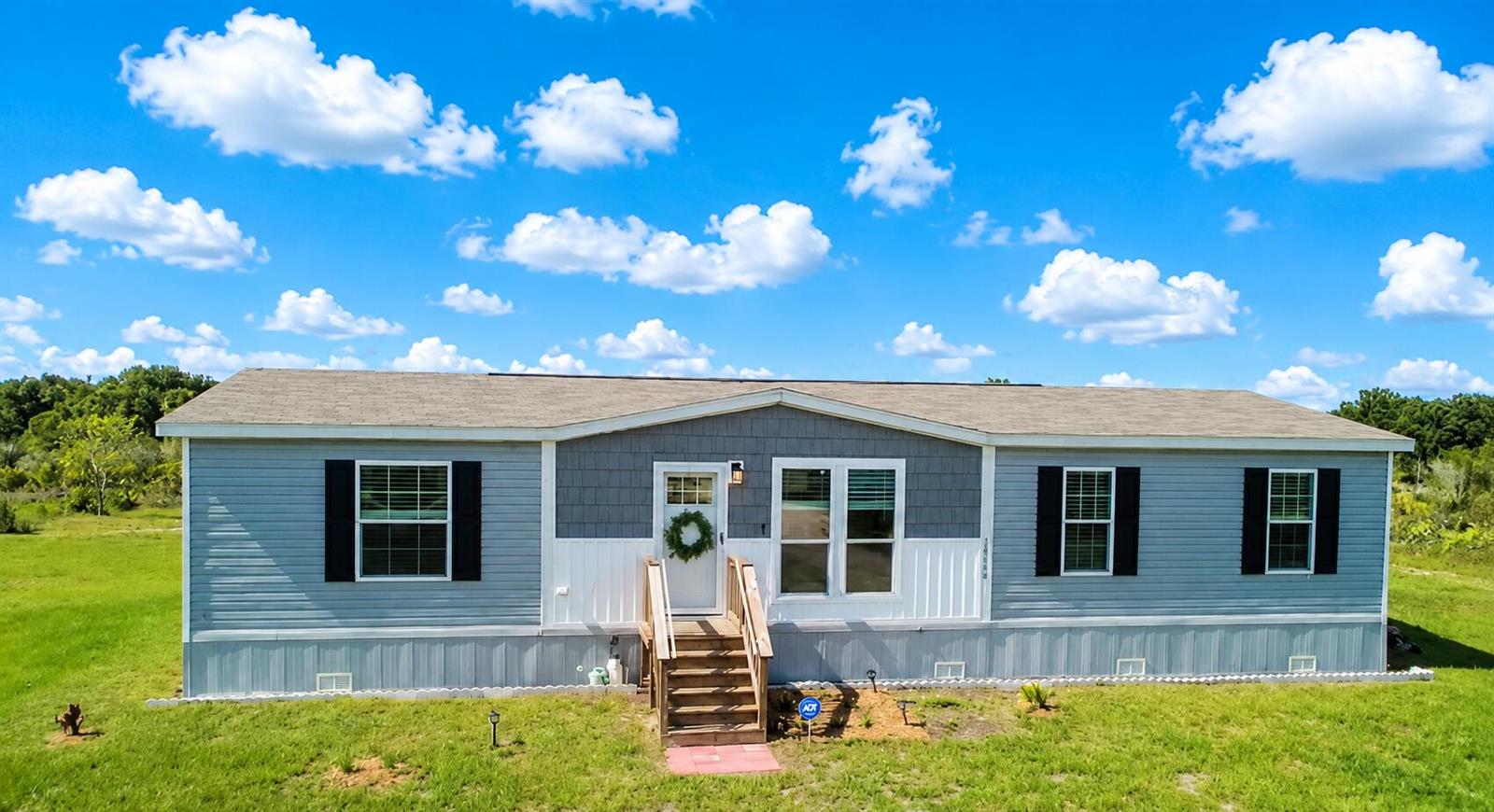 A light blue manufactured home with a gray shingled roof sits on a grassy lot — 18720 NW 242nd Street, Okeechobee FL 34972, OKEECHOBEE, FL