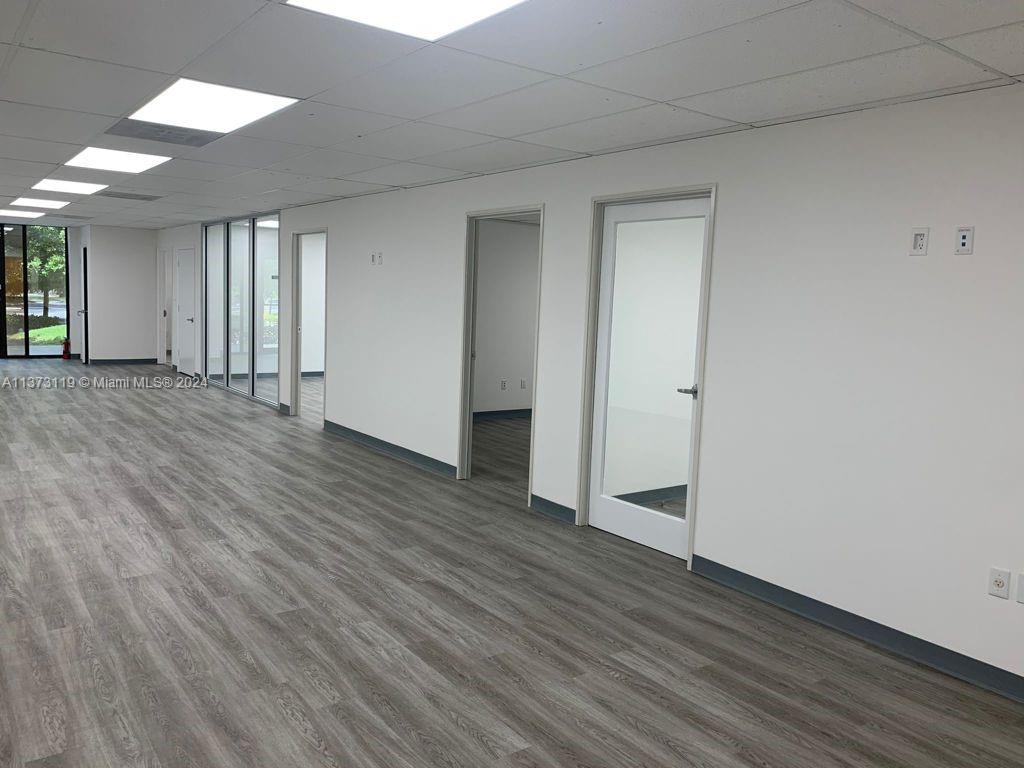 An empty office space features white walls, wood-look flooring, recessed lighting, and several doorways — FORT LAUDERDALE, FL