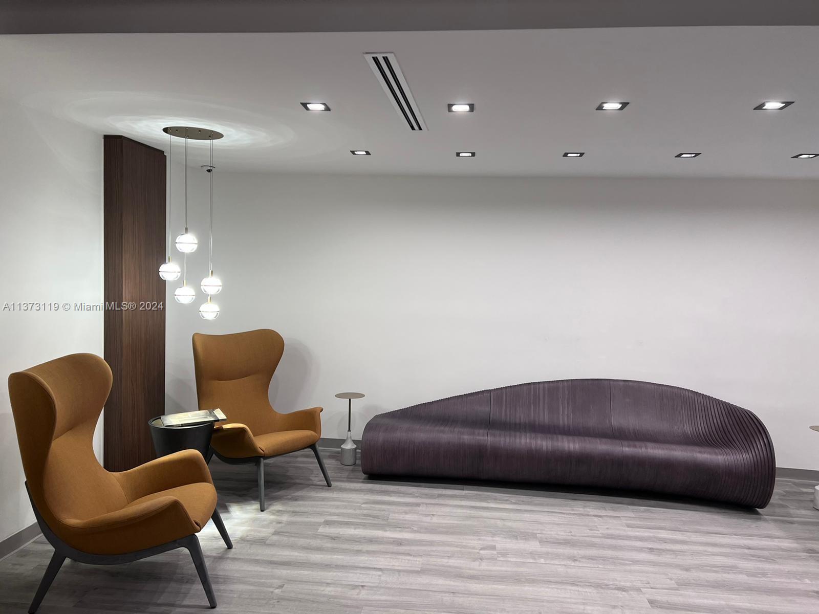 A modern lounge area features two orange wingback chairs, a curved sofa, and pendant lighting — FORT LAUDERDALE, FL