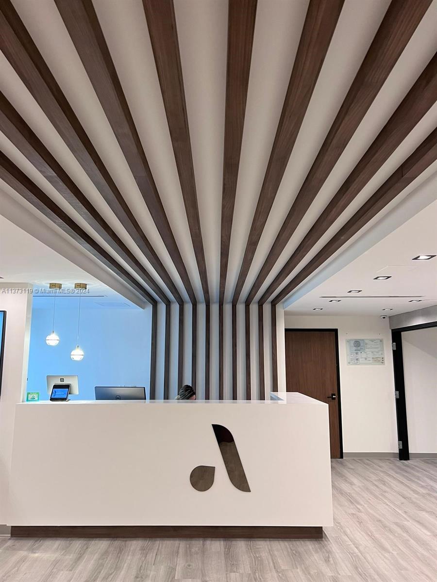 A reception desk with a logo sits beneath a decorative wood-slat ceiling feature — FORT LAUDERDALE, FL