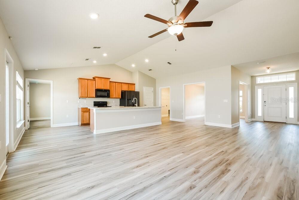 An open-concept living area features light wood-look flooring, a kitchen with wooden cabinets, and recessed lighting — 7803 SLOEWOOD DRIVE, LEESBURG, FL