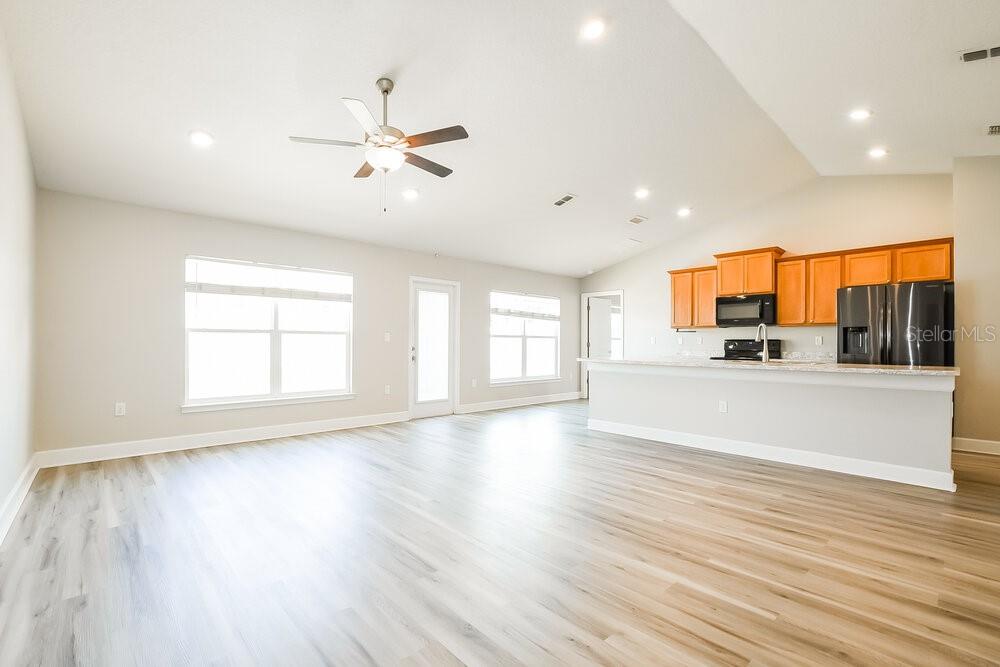 An open-concept living area features light wood-look flooring, a ceiling fan, and a kitchen — 7803 SLOEWOOD DRIVE, LEESBURG, FL