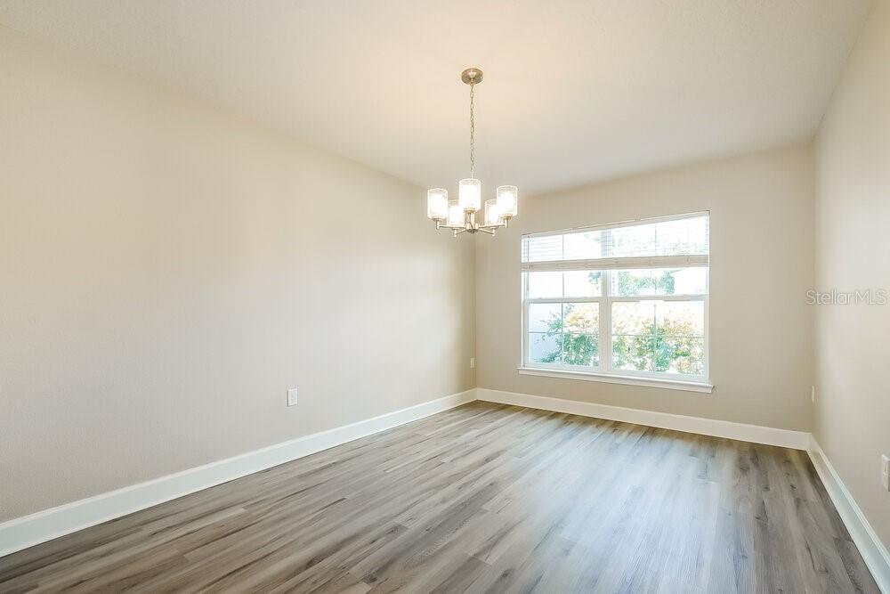 An empty dining room features light-colored walls, a chandelier, and wood-look vinyl plank flooring — 7803 SLOEWOOD DRIVE, LEESBURG, FL