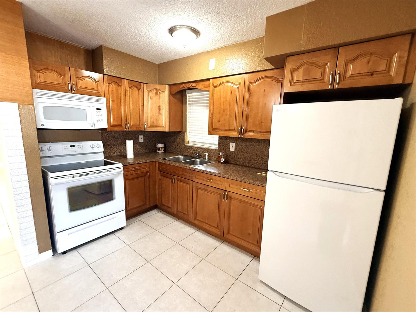 A kitchen features wood cabinets, white appliances, brown countertops, and light-colored tile flooring — 551 SE 15th Street, Pompano Beach FL 33062, POMPANO BEACH, FL