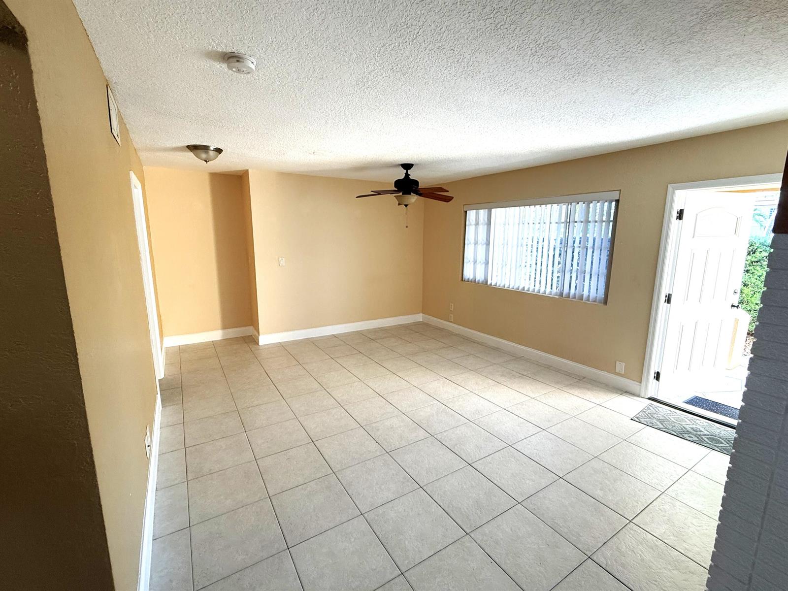 An empty living room features beige walls, light-colored tile flooring, a ceiling fan, and a door — 551 SE 15th Street, Pompano Beach FL 33062, POMPANO BEACH, FL