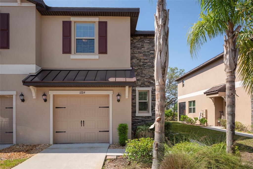 A two-story townhouse exterior features a tan stucco facade, stone accents, and a garage — 11704 CASTINE STREET, NEW PORT RICHEY, FL