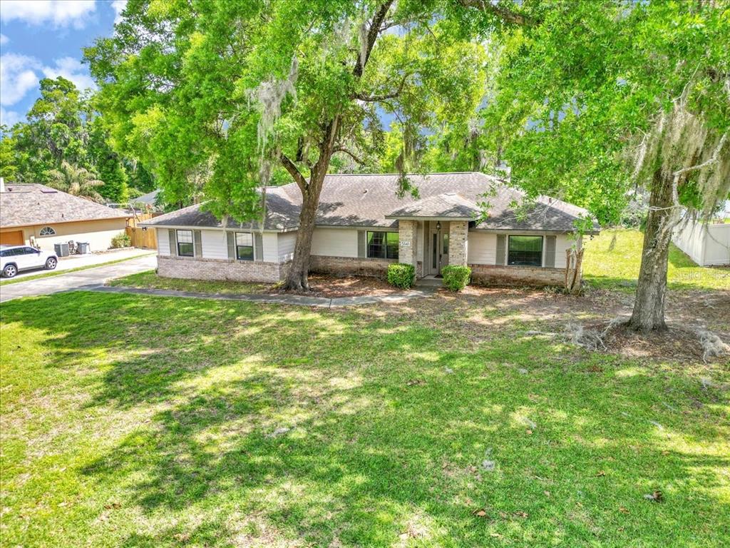 A single-story house with a brick and siding exterior sits behind large trees and grass — 5141 SE 36TH AVENUE, OCALA, FL
