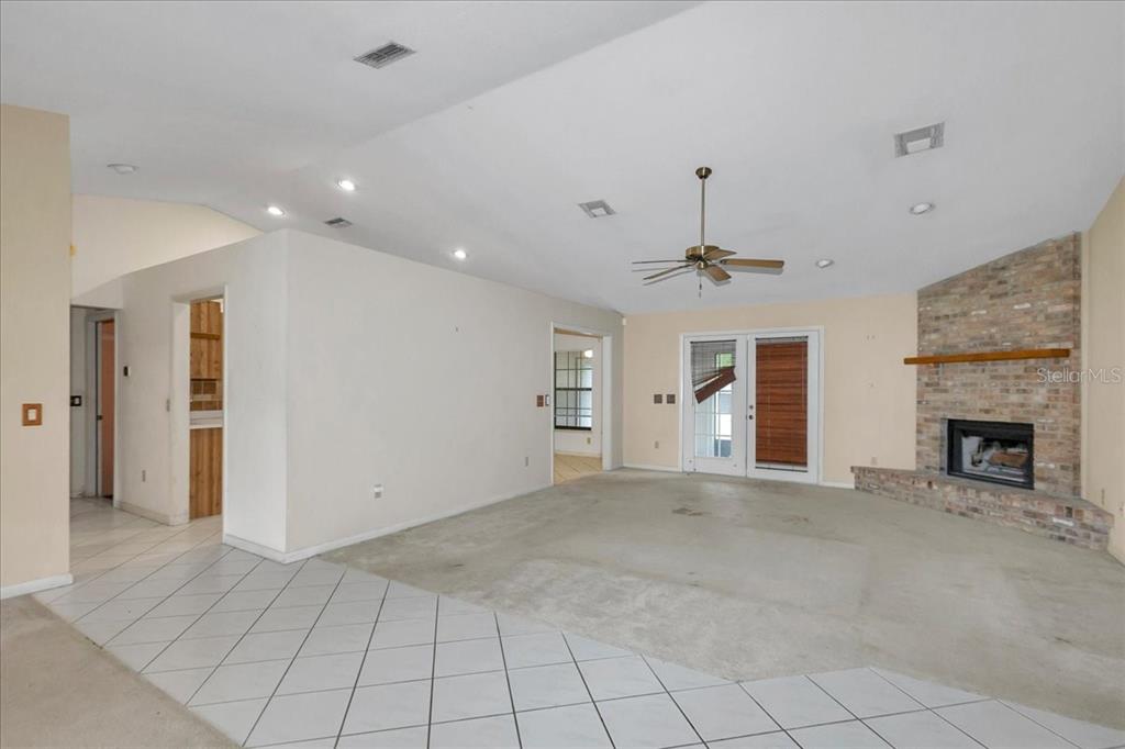 A living room with a brick fireplace, vaulted ceiling, ceiling fan, and tiled entryway — 5141 SE 36TH AVENUE, OCALA, FL