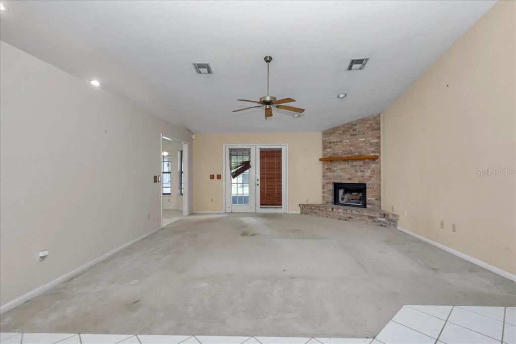 An empty living room features a brick corner fireplace, ceiling fan, and glass patio doors — 5141 SE 36TH AVENUE, OCALA, FL