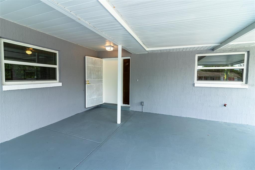 A gray covered patio features a white front door, two windows, and a ceiling light — 474 SPRING LANE, OCALA, FL