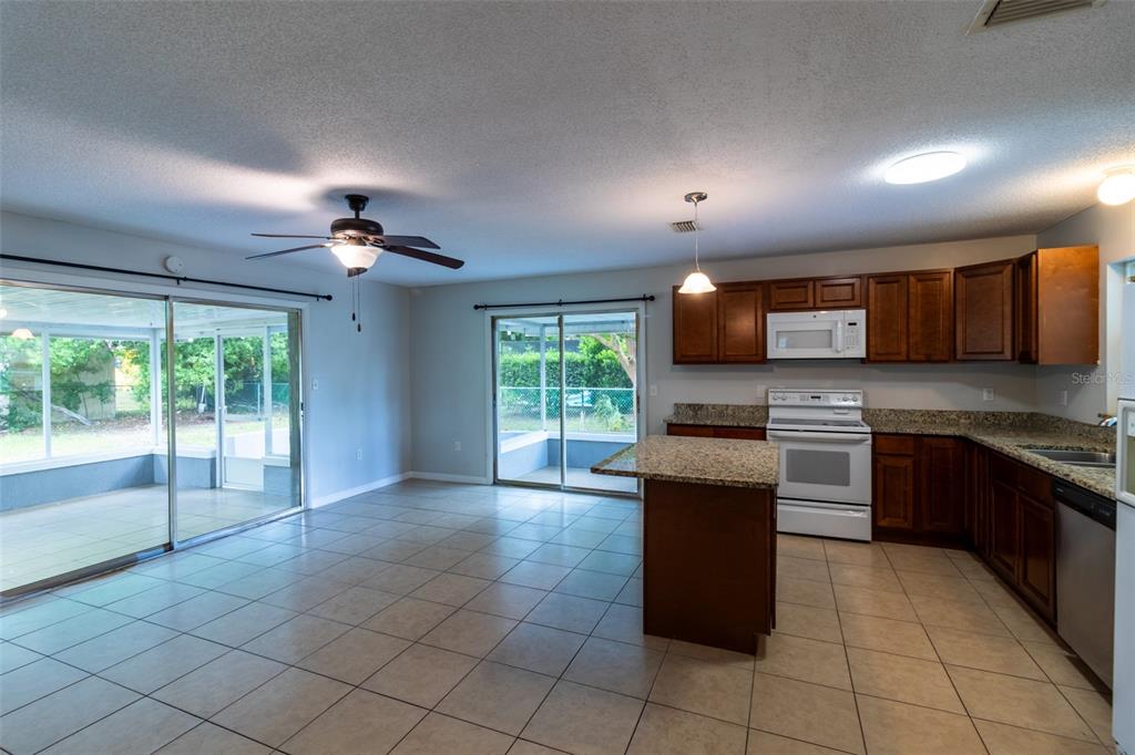 An open-concept kitchen and living area features tile flooring, dark wood cabinets, and granite countertops — 474 SPRING LANE, OCALA, FL