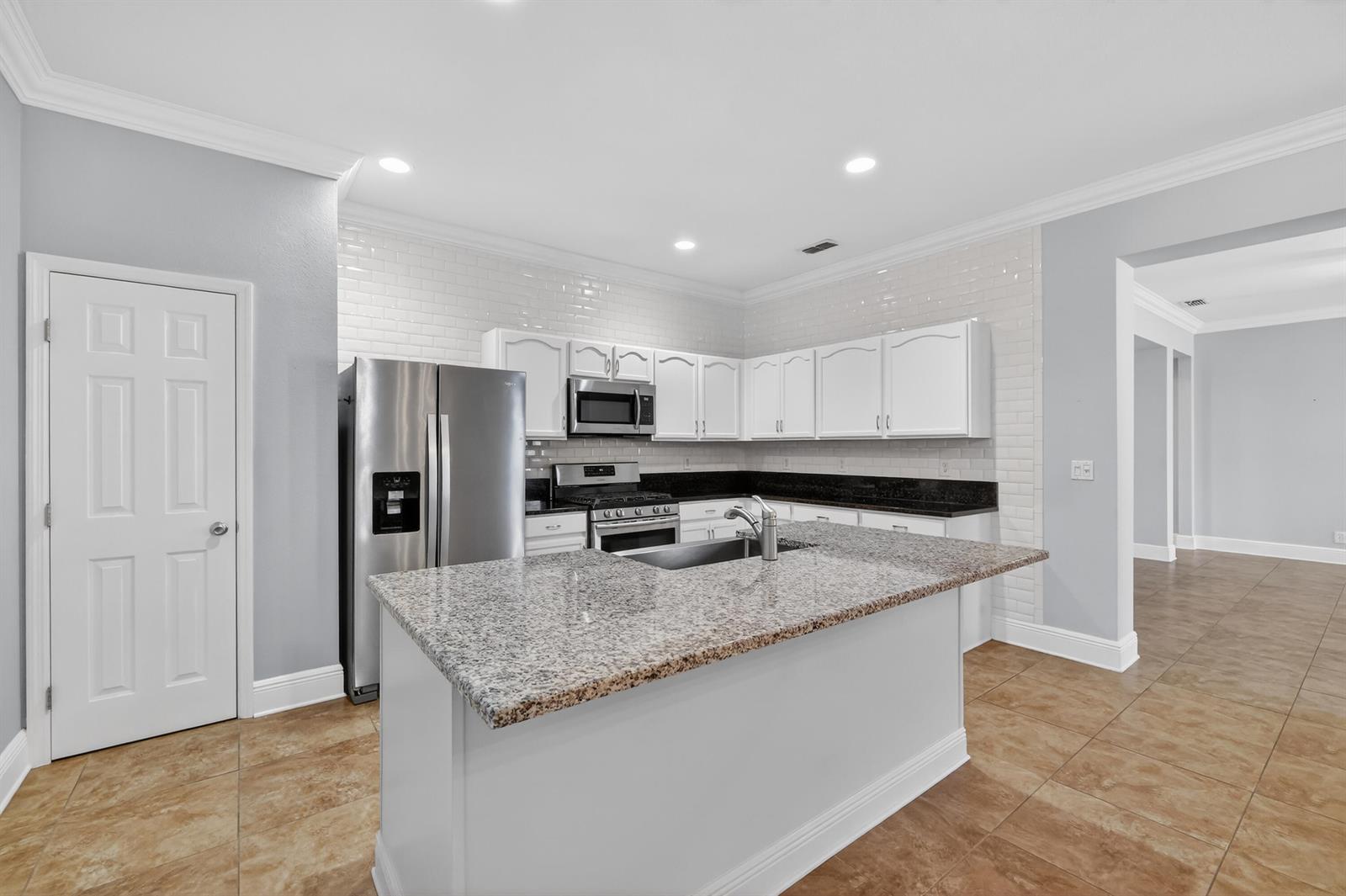 A kitchen features white cabinets, granite countertops, a center island, and a subway tile backsplash — 7865 15th Lane, Vero Beach FL 32966, VERO BEACH, FL