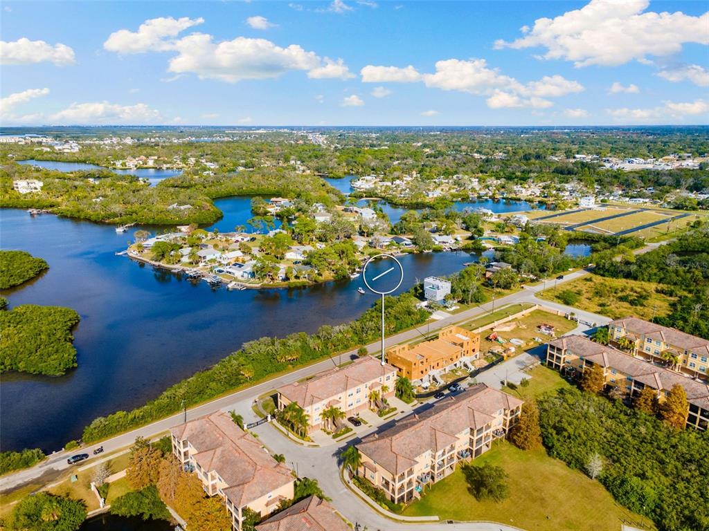 An aerial view shows multi-story apartment buildings situated near a coastal waterway and mangroves — 4533 HERON LODGE, NEW PORT RICHEY, FL