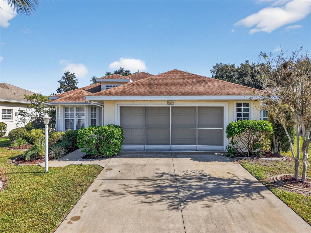A single-story house with a tan exterior, a brown shingled roof, and a screened garage — 21202 BRAVEHEART DRIVE, LEESBURG, FL