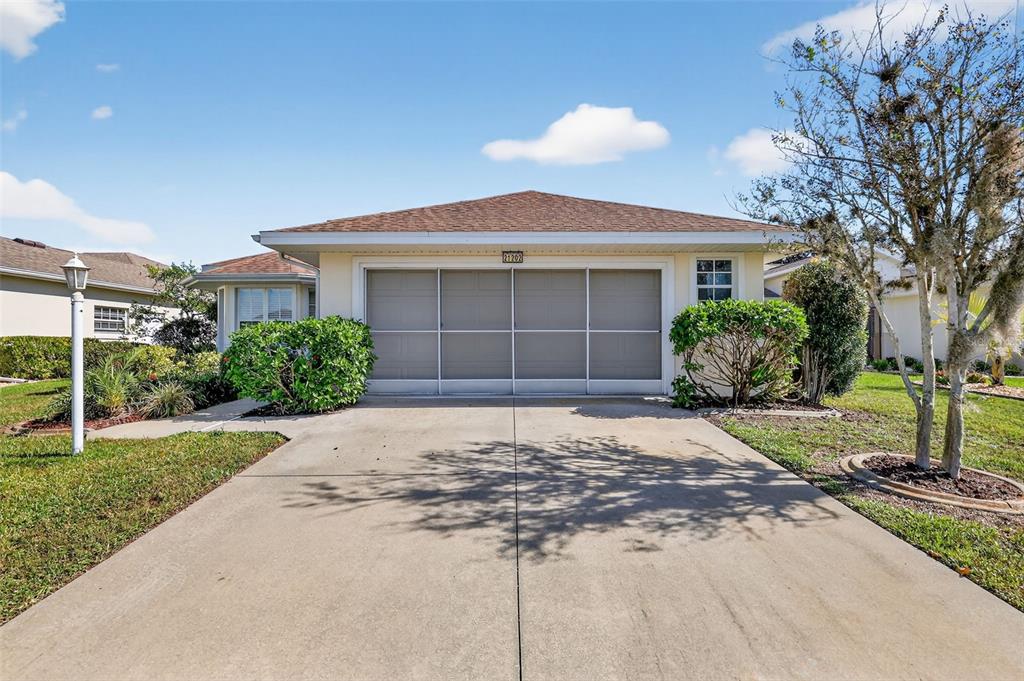 A single-story house features a concrete driveway leading to a screened-in garage door — 21202 BRAVEHEART DRIVE, LEESBURG, FL