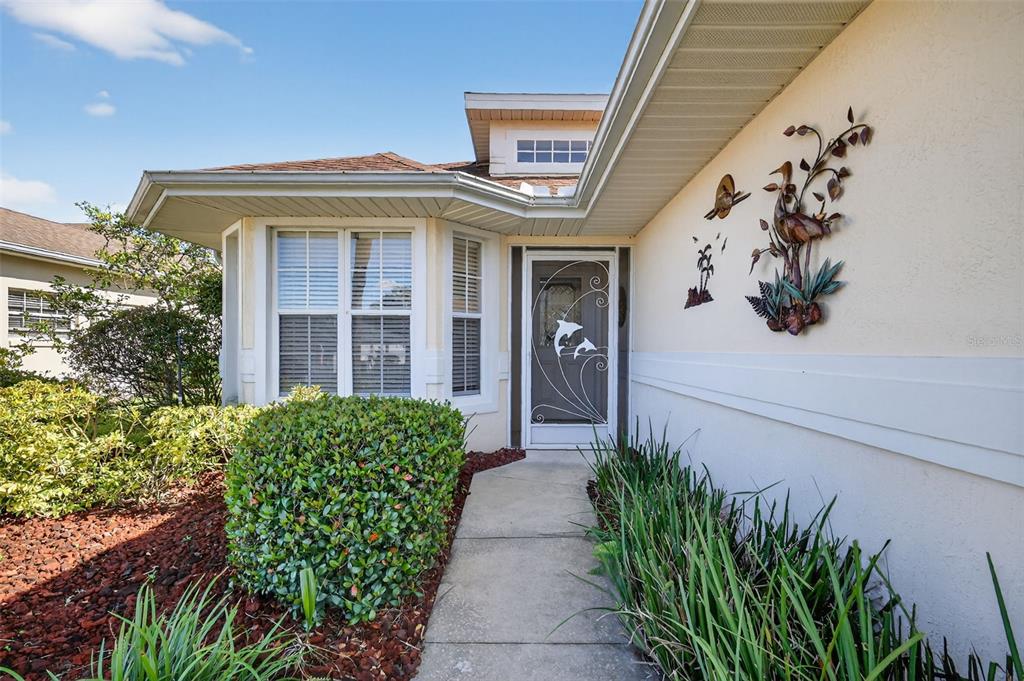 A sidewalk leads to the front entrance of a house with a dolphin-decorated screen door — 21202 BRAVEHEART DRIVE, LEESBURG, FL