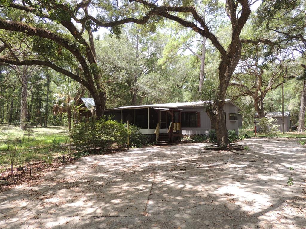 A single-story house with a screened porch sits on a concrete lot among large trees — 7850 NE 178TH TERRACE, WILLISTON, FL