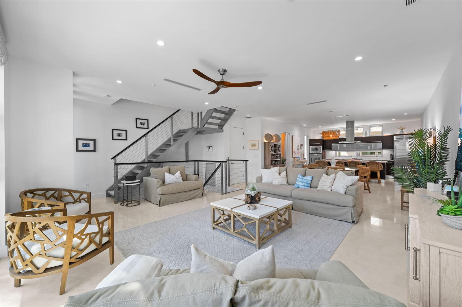 A spacious open-concept living room features a modern staircase, neutral furniture, and a kitchen area — 705 Briny Avenue, Pompano Beach FL 33062, POMPANO BEACH, FL