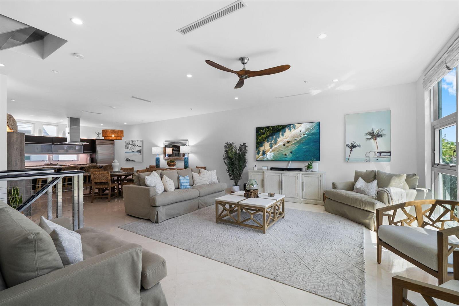 A bright, open-concept living room features neutral furniture, a large area rug, and a kitchen — 705 Briny Avenue, Pompano Beach FL 33062, POMPANO BEACH, FL