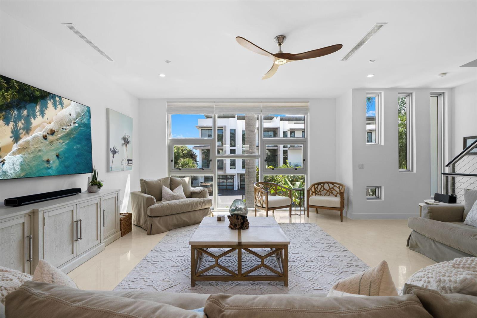 A bright living room features a large television, neutral furniture, and floor-to-ceiling windows — 705 Briny Avenue, Pompano Beach FL 33062, POMPANO BEACH, FL