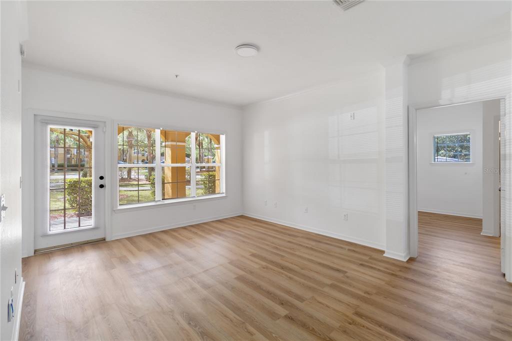 An empty living room with light wood-look flooring, white walls, and a glass-paned exterior door — 3599 CONROY ROAD UNIT 915, ORLANDO, FL