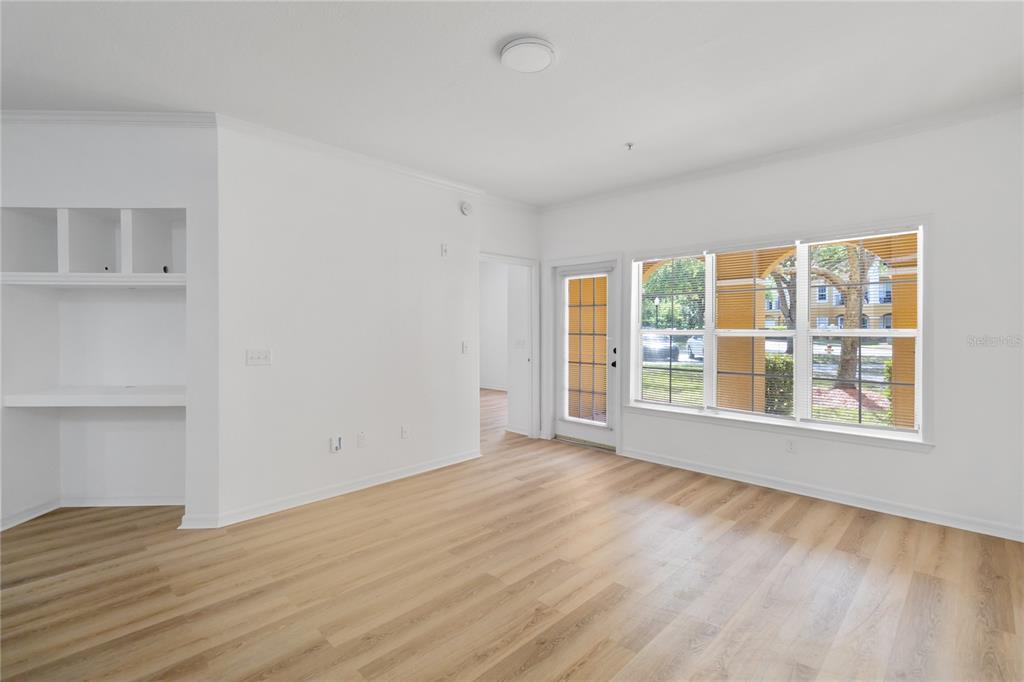 An empty room with light wood-look flooring, white walls, built-in shelving, and large windows — 3599 CONROY ROAD UNIT 915, ORLANDO, FL