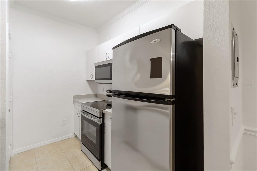 A kitchen features stainless steel appliances, white cabinetry, and light-colored tile flooring — 3599 CONROY ROAD UNIT 915, ORLANDO, FL