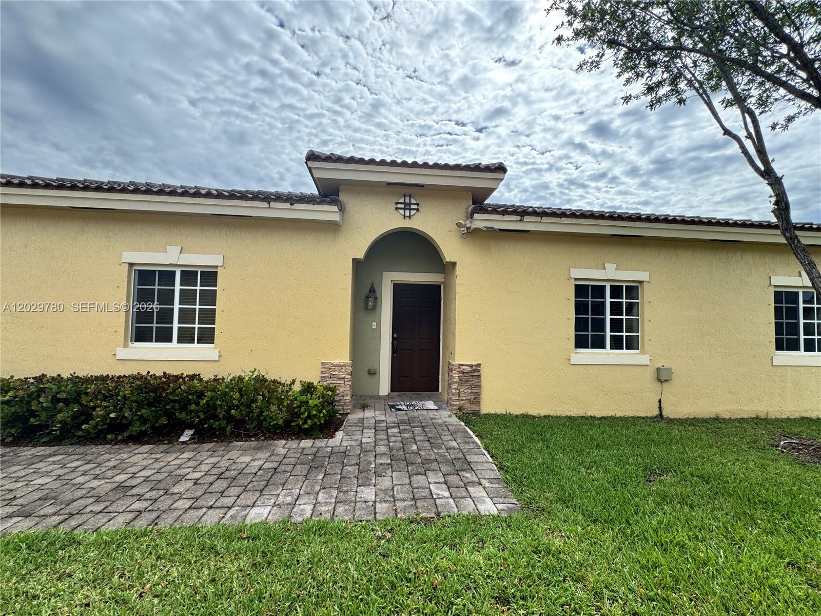 The exterior of a yellow stucco house features a brown front door and tiled roof — 3384 NE 11th Dr, Homestead FL 33033, HOMESTEAD, FL