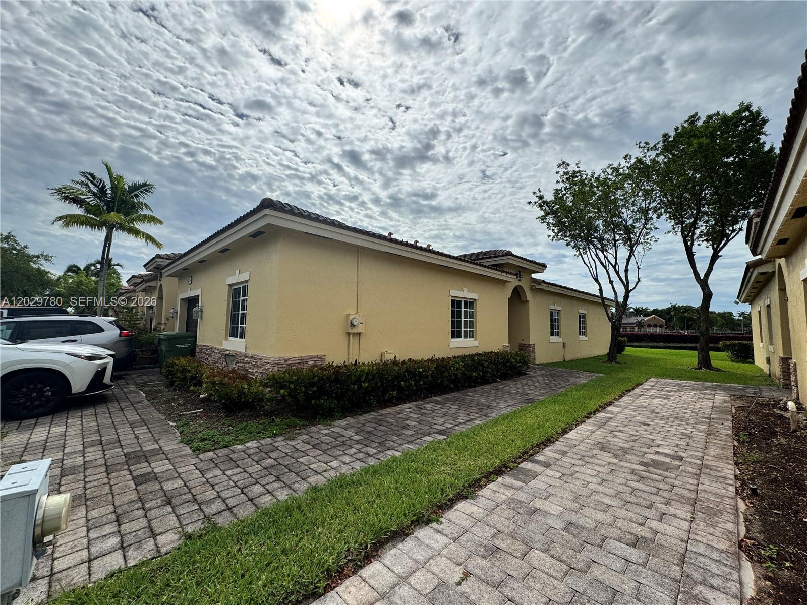 The exterior of a tan stucco house features a paver driveway and a small lawn — 3384 NE 11th Dr, Homestead FL 33033, HOMESTEAD, FL