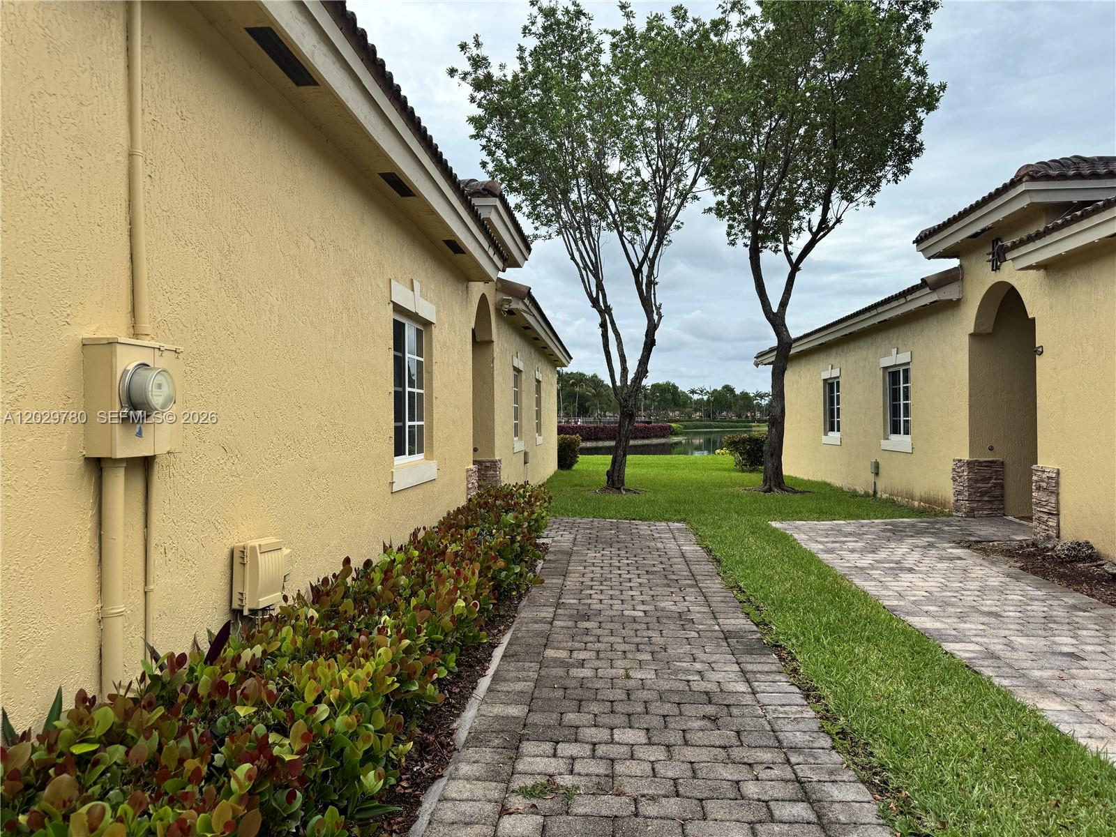 Two yellow stucco houses face each other across a brick walkway leading toward a lake — 3384 NE 11th Dr, Homestead FL 33033, HOMESTEAD, FL