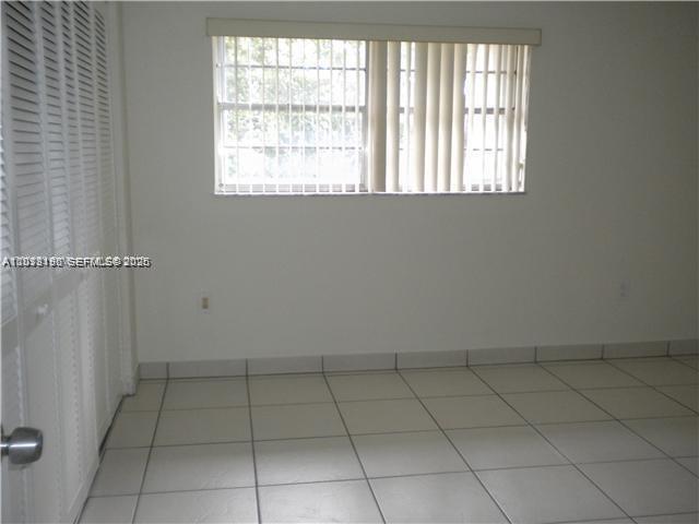 An empty room features white walls, light-colored tile flooring, and a window with vertical blinds — 260 NW 107th Ave # 207, Miami FL 33172, MIAMI, FL