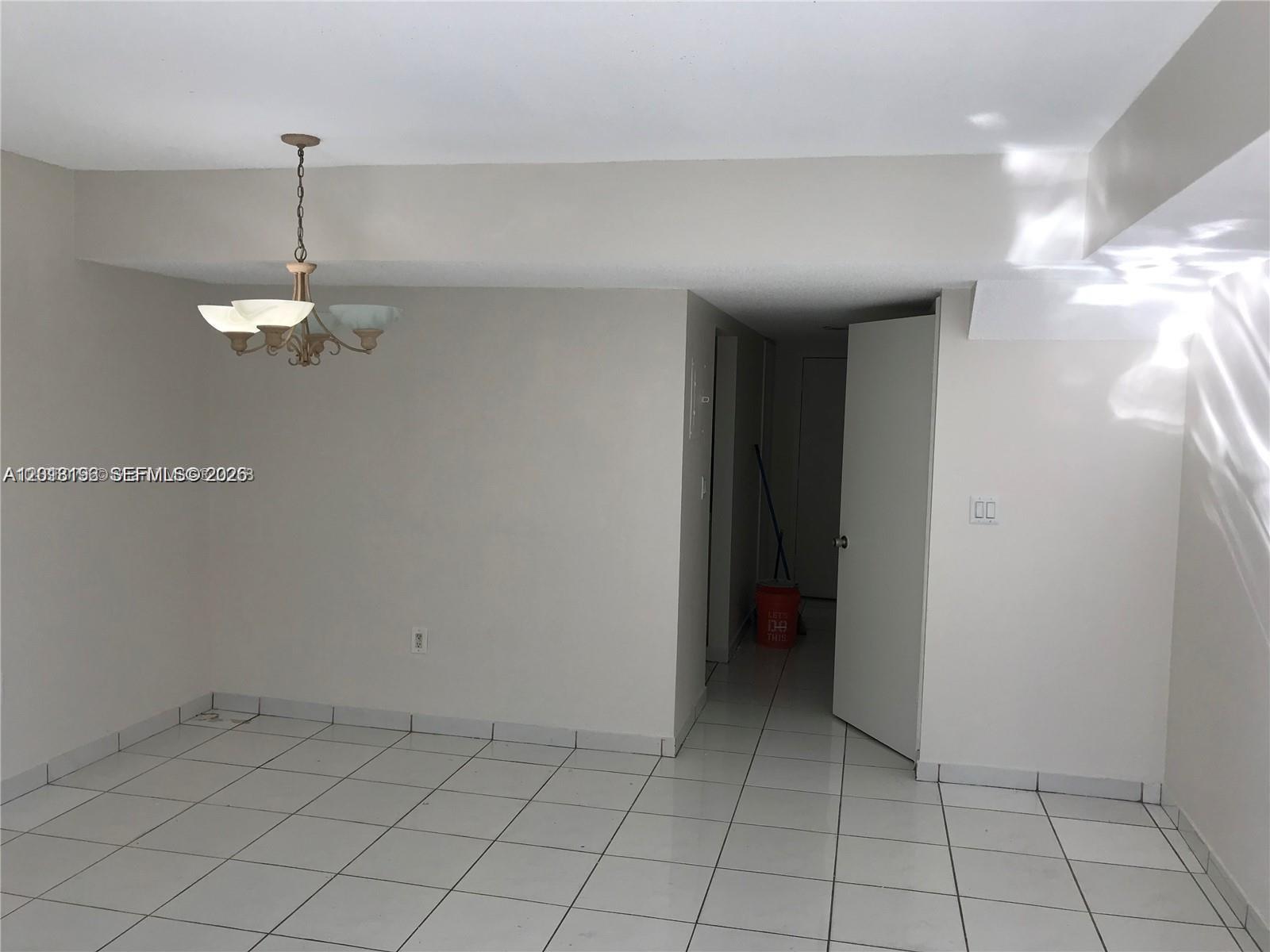 A room with white tile floors, a chandelier, and an open doorway leading to a hallway — 260 NW 107th Ave # 207, Miami FL 33172, MIAMI, FL