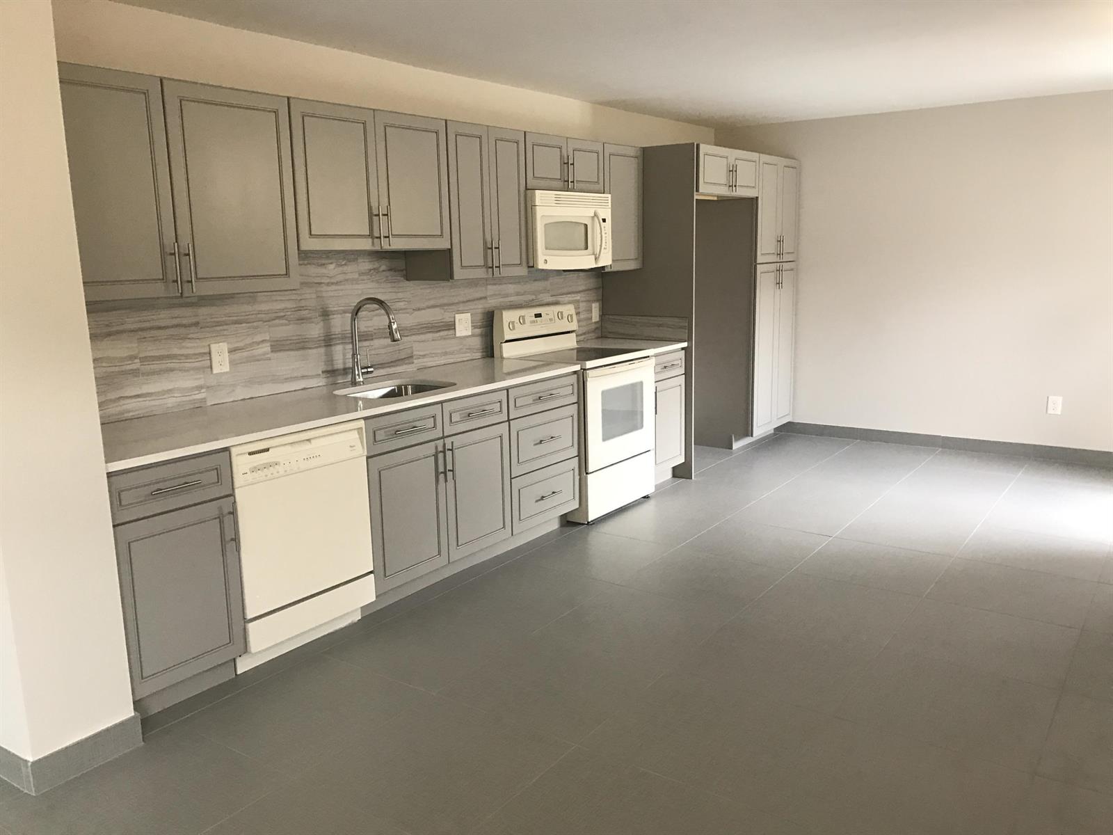 A kitchen features gray cabinets, white appliances, a stone-look backsplash, and gray tile flooring — 142 SW 8th Avenue Apt D, Delray Beach FL 33444, DELRAY BEACH, FL
