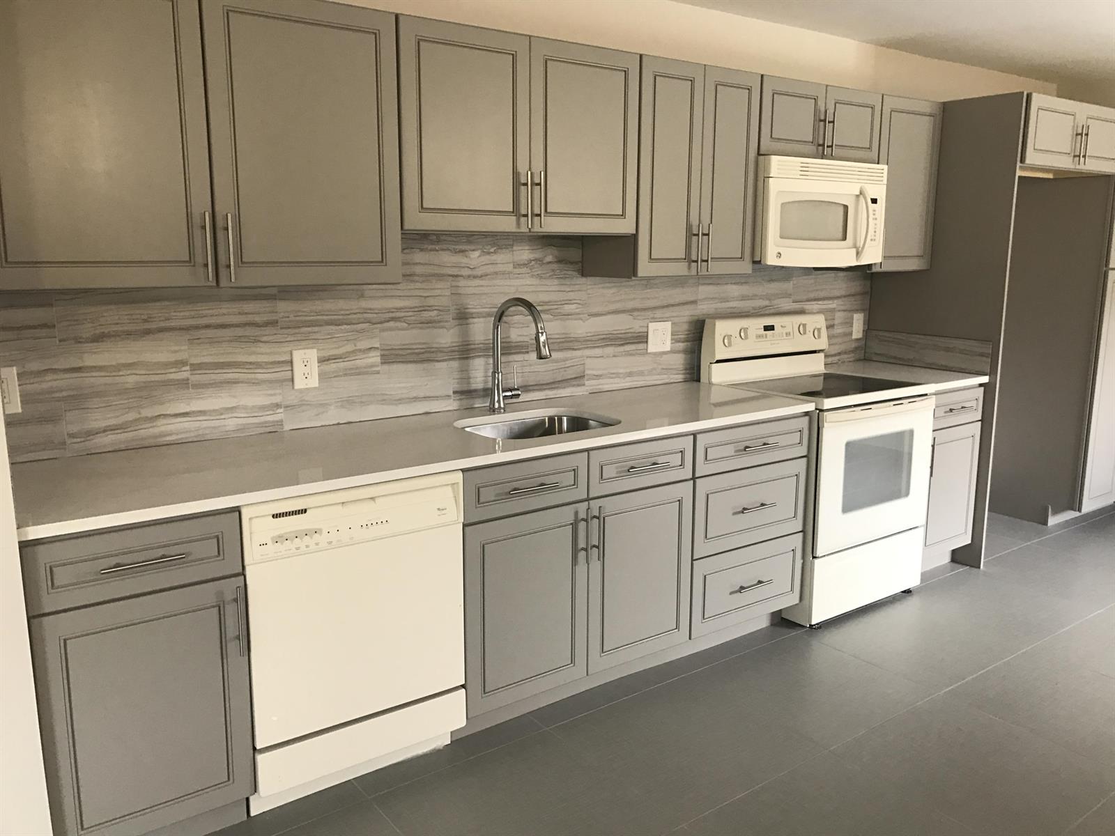 A kitchen features gray shaker cabinets, white appliances, a stone-look backsplash, and light countertops — 142 SW 8th Avenue Apt D, Delray Beach FL 33444, DELRAY BEACH, FL