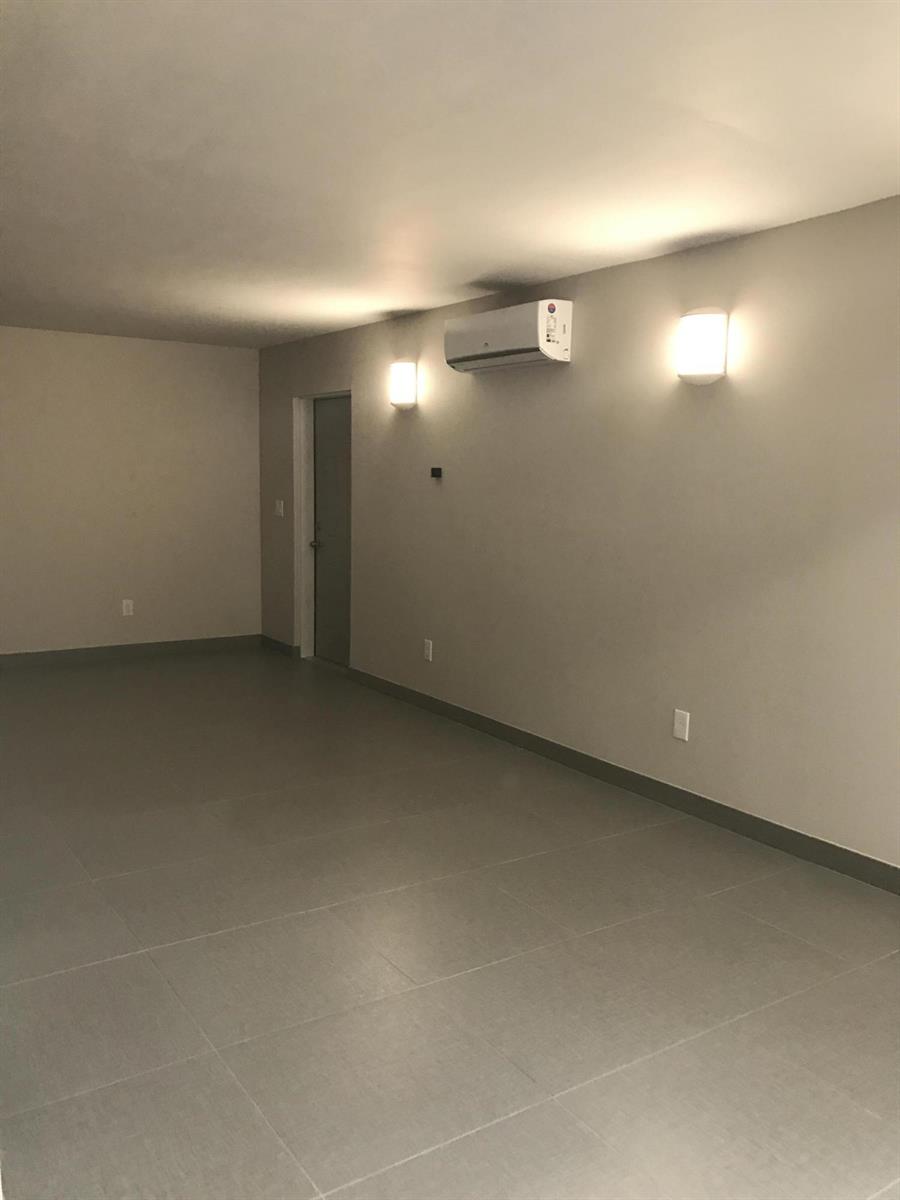 An empty room features gray tile flooring, light-colored walls, two wall sconces, and an air conditioner — 142 SW 8th Avenue Apt D, Delray Beach FL 33444, DELRAY BEACH, FL