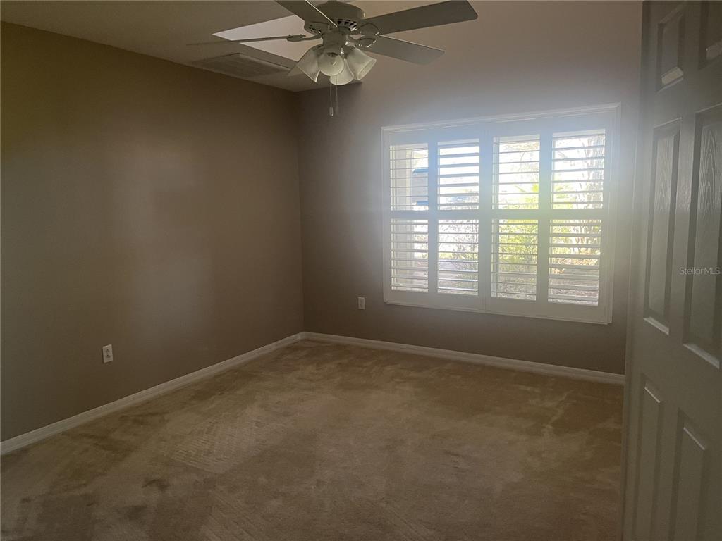 An empty bedroom features beige carpet, brown walls, a ceiling fan, and plantation shutters — 26601 BULL RUN, LEESBURG, FL