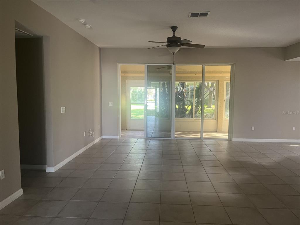 An open living area features neutral tile flooring, a ceiling fan, and sliding glass doors — 26601 BULL RUN, LEESBURG, FL