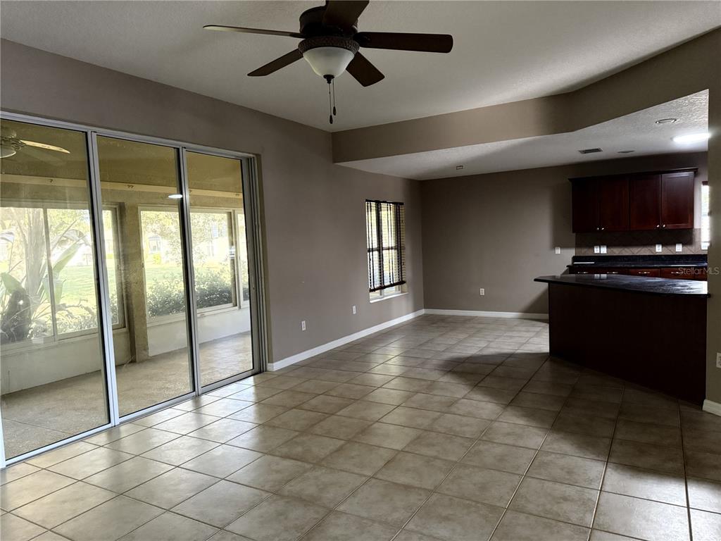 A room with tile flooring, a ceiling fan, sliding glass doors, and an open kitchen — 26601 BULL RUN, LEESBURG, FL