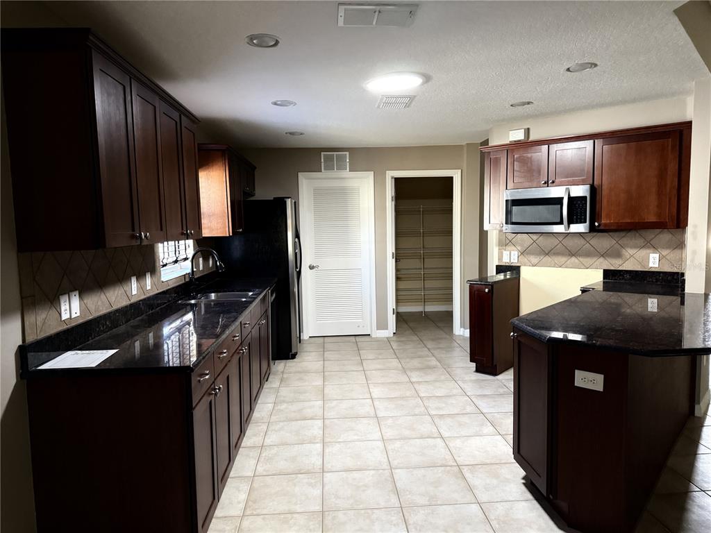 A kitchen features dark wood cabinets, black granite countertops, stainless steel appliances, and tile flooring — 26601 BULL RUN, LEESBURG, FL