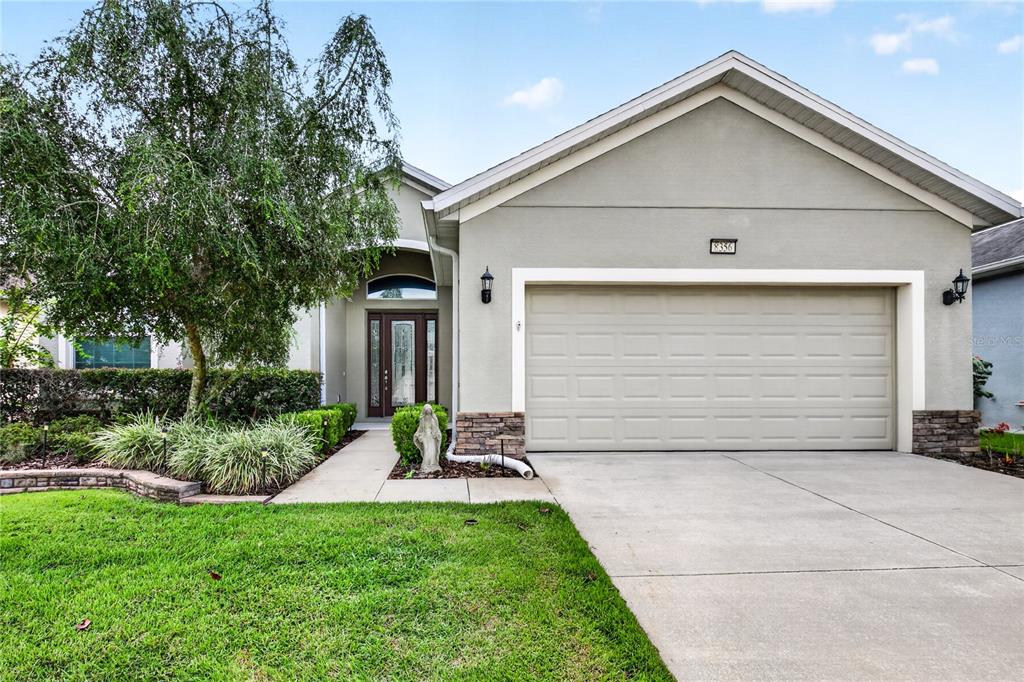A single-story suburban house features a two-car garage, stone accents, and a landscaped front yard — 8356 BRIDGEPORT BAY CIRCLE, MOUNT DORA, FL