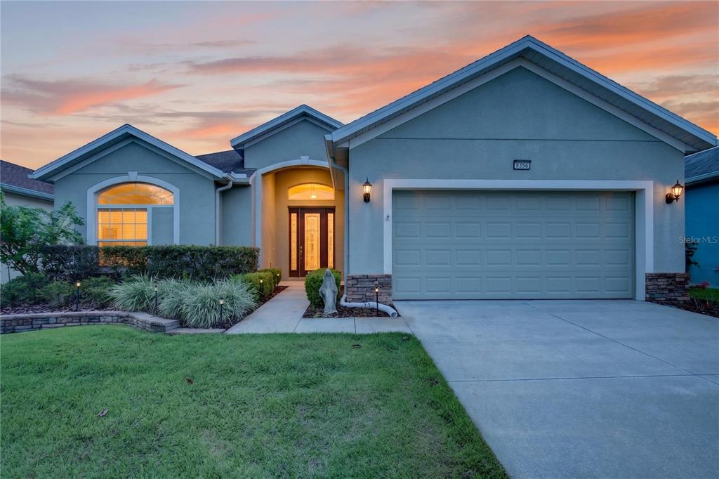 A single-story house with a two-car garage, arched entryway, and a green stucco exterior — 8356 BRIDGEPORT BAY CIRCLE, MOUNT DORA, FL