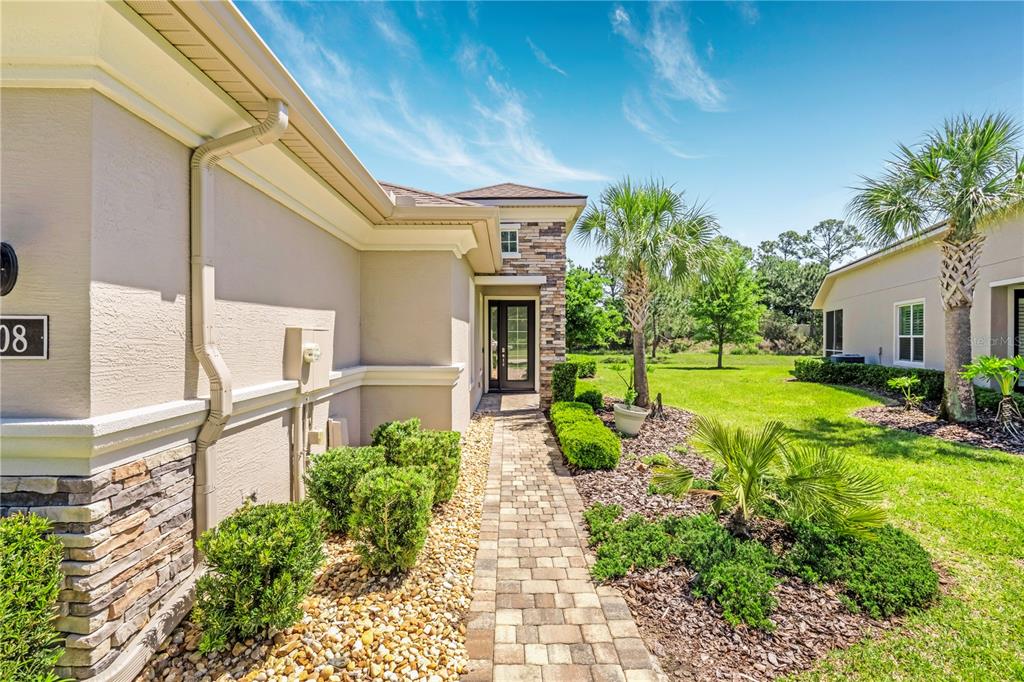 A paved walkway leads to the front entrance of a house with stone accents — 708 ALDENHAM LANE, ORMOND BEACH, FL