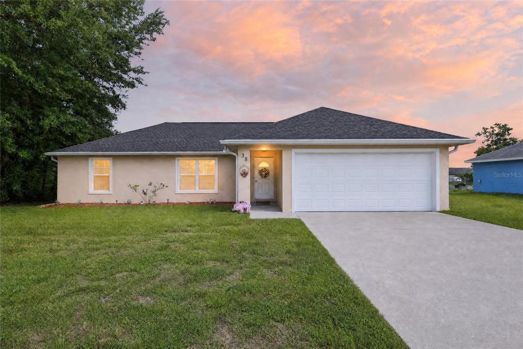 A single-story house with a tan stucco exterior, a white garage door, and a lawn — 38 JUNIPER LOOP COURT, OCALA, FL
