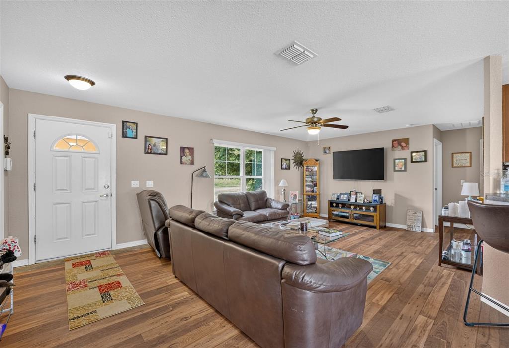 A living room features brown leather sofas, wood-look flooring, a ceiling fan, and a television — 38 JUNIPER LOOP COURT, OCALA, FL