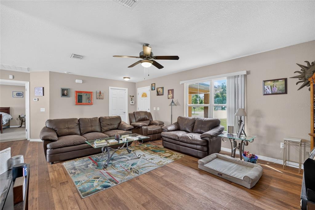 A living room with brown leather furniture, a glass coffee table, and wood-look flooring — 38 JUNIPER LOOP COURT, OCALA, FL