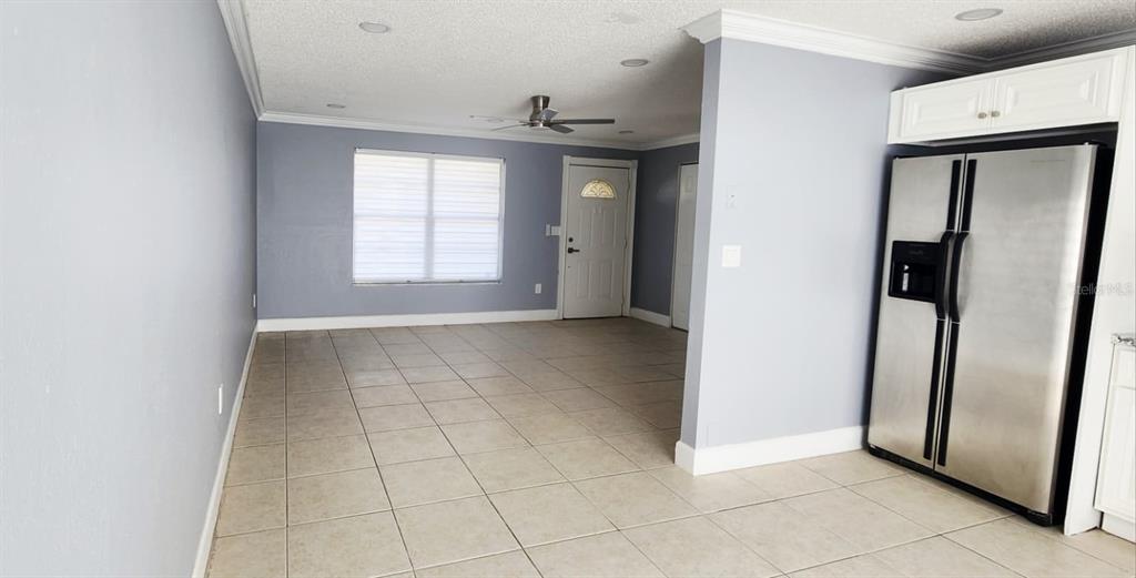 An open-concept room features light-colored tile flooring, gray walls, and a stainless steel refrigerator — 7118 JENNER AVENUE, NEW PORT RICHEY, FL