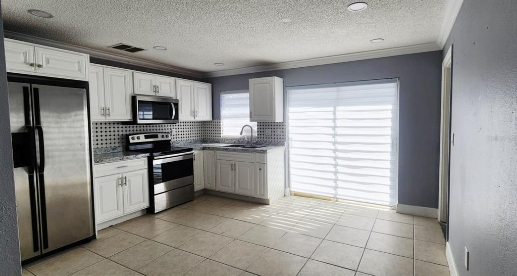 A kitchen with white cabinets, stainless steel appliances, a tiled backsplash, and light-colored floor tiles — 7118 JENNER AVENUE, NEW PORT RICHEY, FL