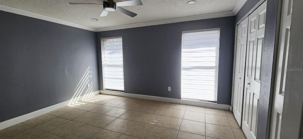 A bedroom with gray walls, tiled flooring, a ceiling fan, and white closet doors — 7118 JENNER AVENUE, NEW PORT RICHEY, FL