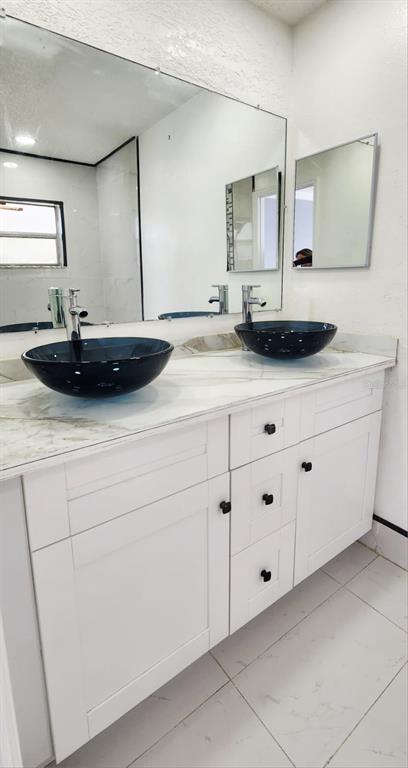 A bathroom vanity with two black vessel sinks, white cabinets, and a large wall mirror — 7118 JENNER AVENUE, NEW PORT RICHEY, FL