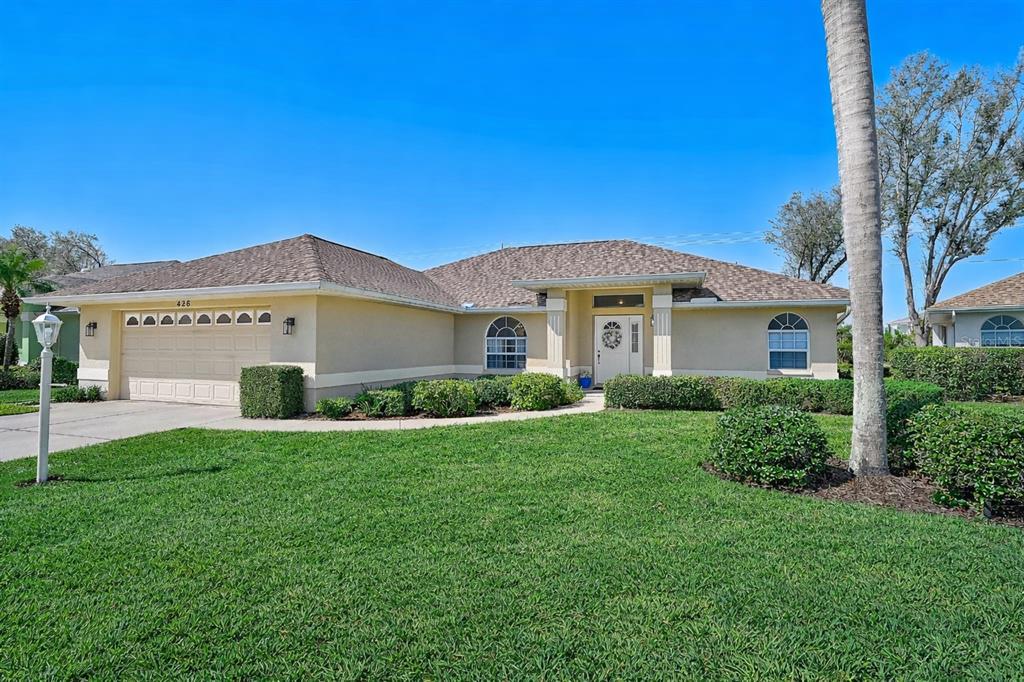 A single-story suburban house with a tan stucco exterior, a two-car garage, and a lawn — 426 BERMUDA ISLES CIRCLE, VENICE, FL